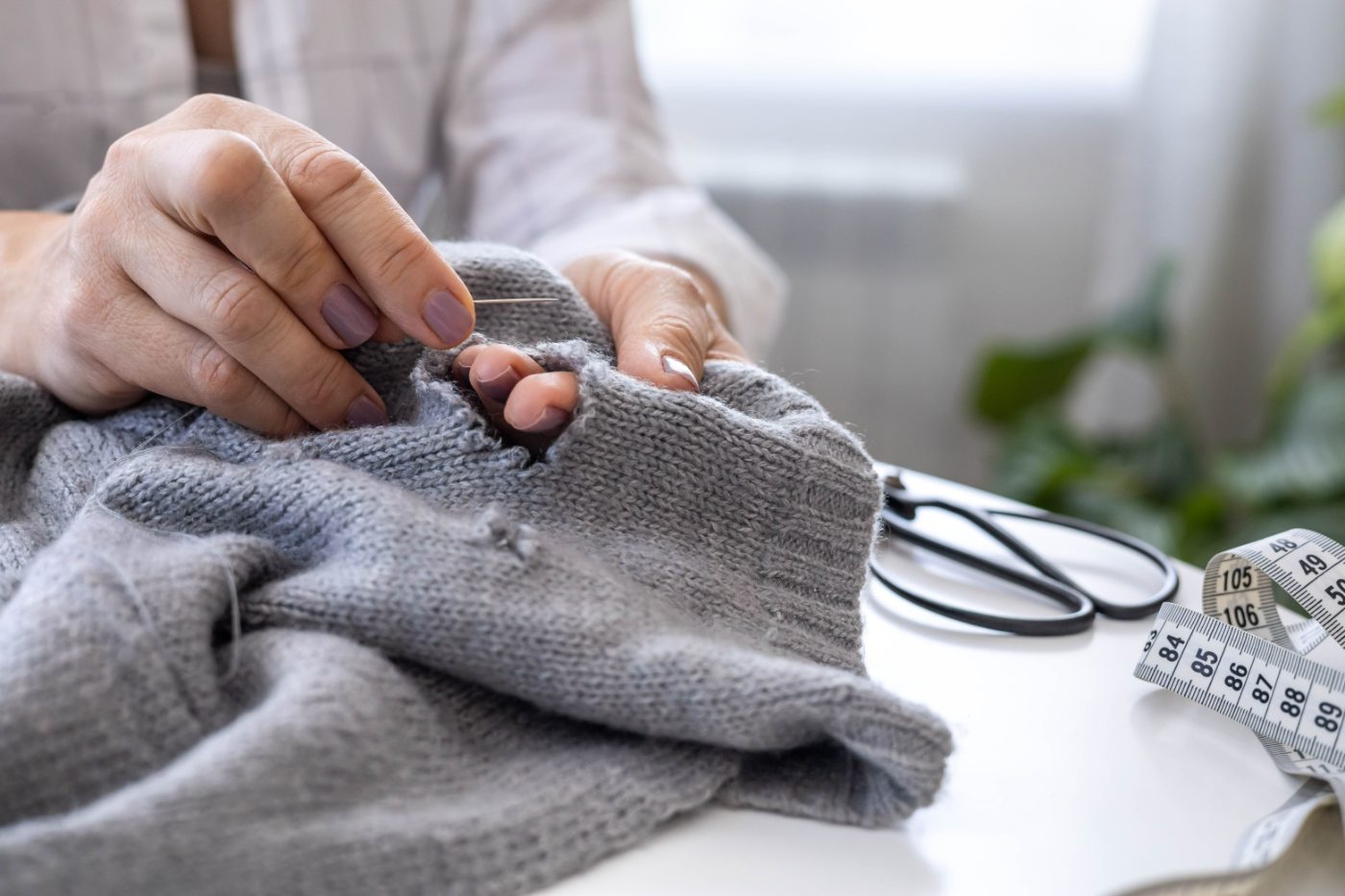 Hands repairing a grey knitted jumper with needle and thread