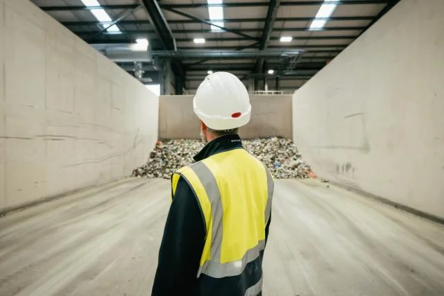 A worker in a hard hat and hi-vis vest looking at sorted recyclables in a materials recovery facility