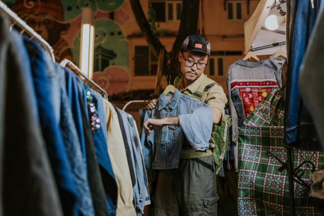 A shopper inspecting a denim jacket at a second-hand clothing market