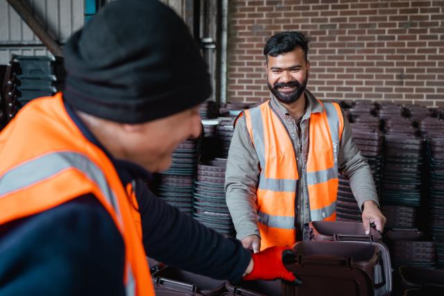 Two council waste operatives in hi-vis handling recycling containers at a depot